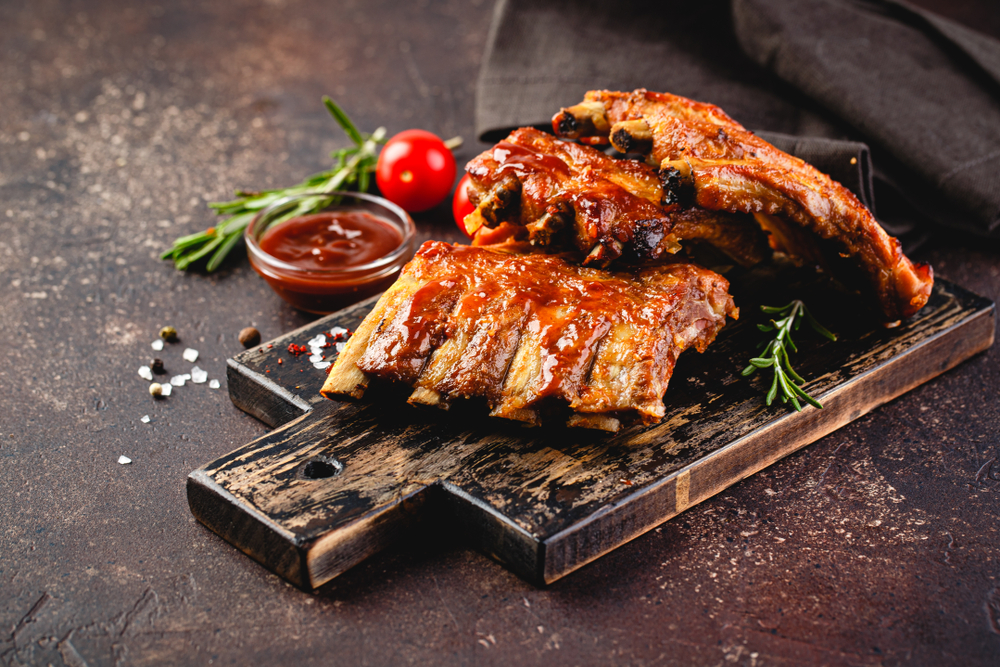 Grilled pork ribs on a wooden cutting board on a brown background