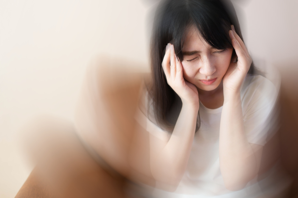 Young female suffering from dizziness, vertigo, headache while sitting on couch at home. Cause of dizzy inclued migraine, stress, stroke, BPPV, Meniere’s disease or brain tumor. Health care problem.