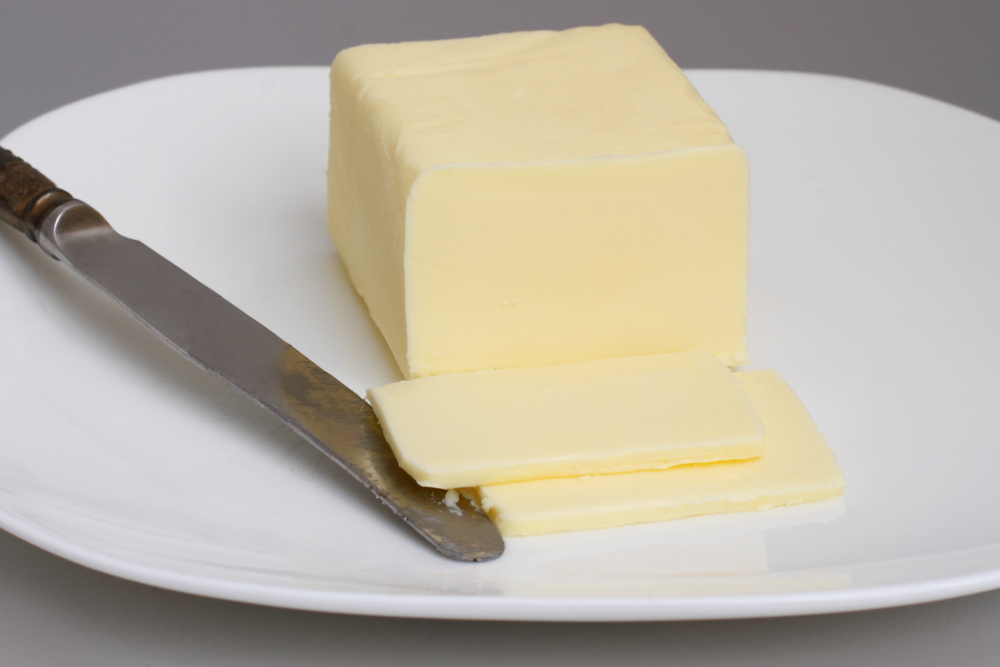 block creamy butter cut on a white plate with a knife
