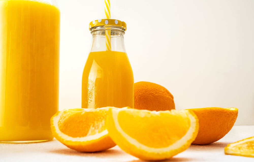 Fresh juicy orange slices and bottles with orange juice on a white background. Misty bottle with drops of condensate with a yellow screw cap and a striped cocktail tube. Close-up