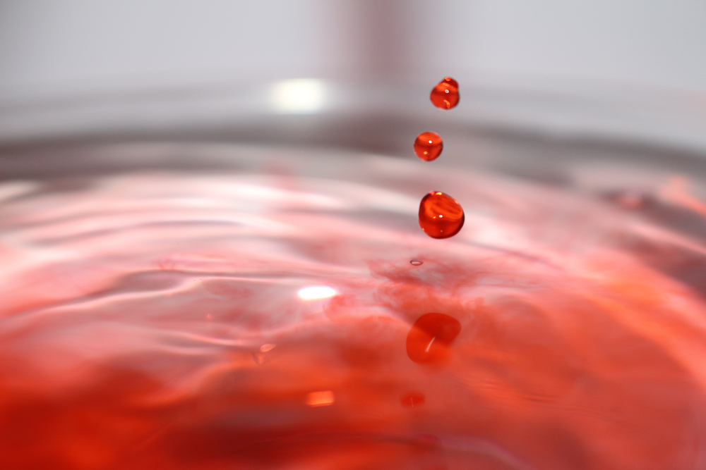 Three drops with red dye falling under reddish water