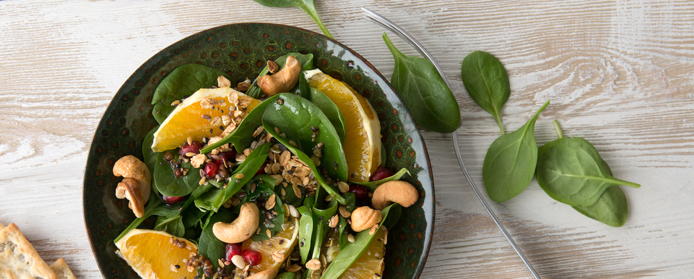 flat lay bowl with spinach, orange and cashew salad on light wooden table