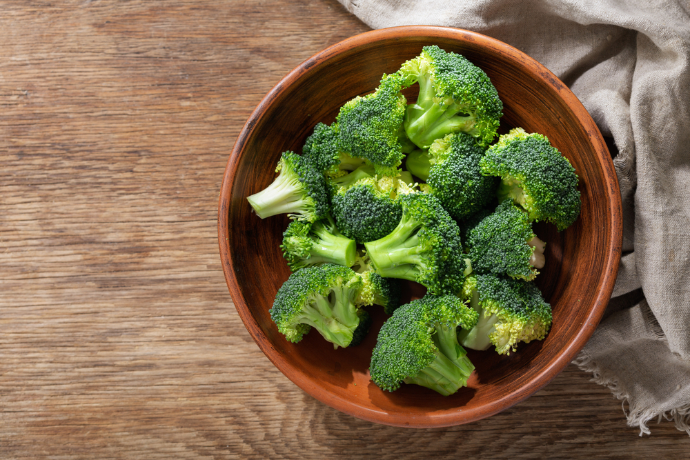 Bowl of fresh broccoli florets on wooden background, top view
