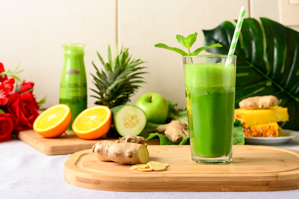 detox green juice, glass with green juice on a wooden board, small fruit ingredient for the juice next to the glass with the drink
