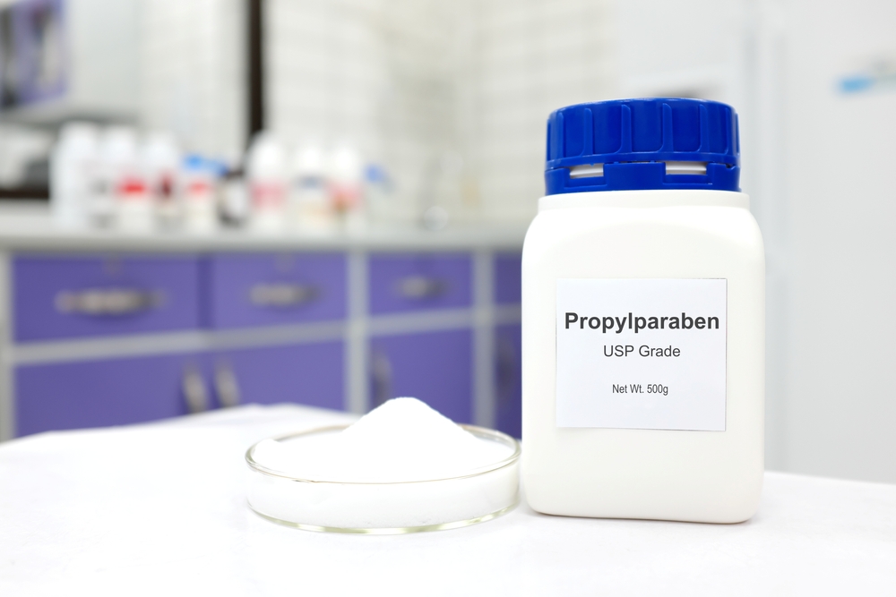 Selective focus of a bottle of Propylparaben paraben pure chemical compound used as preservative in cosmetics and pharmaceutical products. White laboratory background.