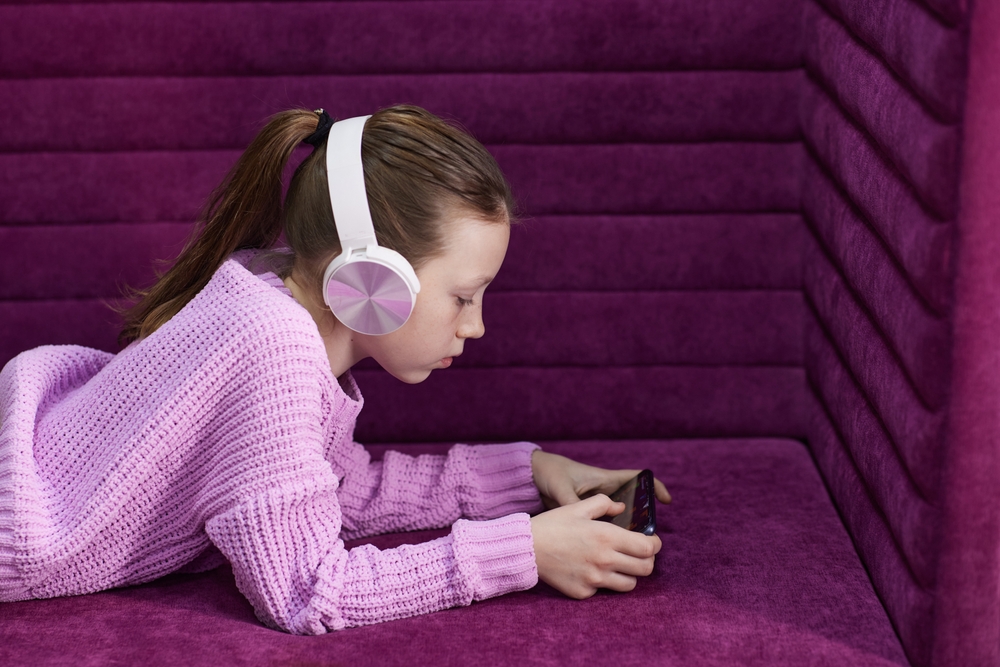 little girl plays in a children's room with headphones and a smartphone. using a mobile phone with a headset and watching videos at home. Girl's homework using the app