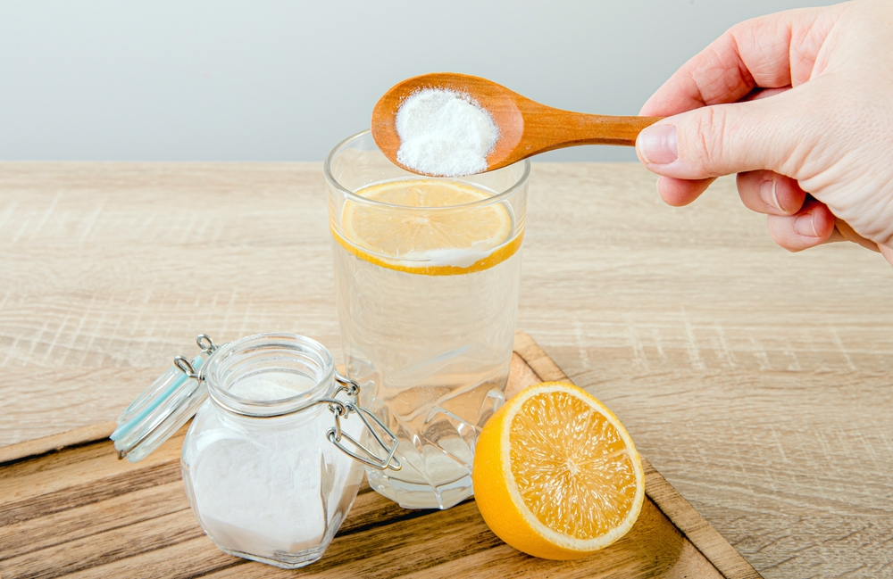 Close up of woman hand pouring baking soda in drinking glass with water and lemon juice, health benefits for digestive system concept.
