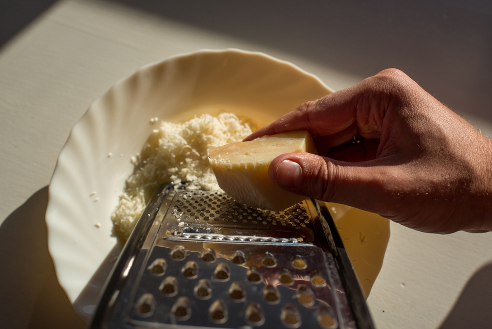 Man grating hard cheese. Ggrater and a plate with grated hard tasty cheese on a light background. Dairy. Concept: Italian cuisine, cheese, restaurant and food. Copy space