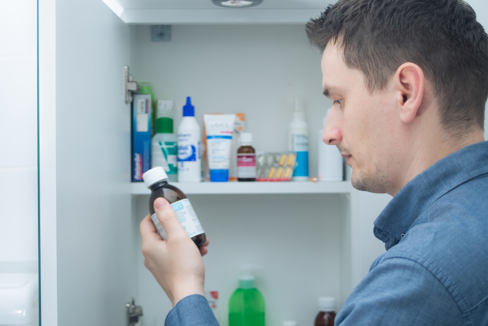 Man hold medication bottle reading instruction or prescription on packaging. Man looking at bottles from medicine cabinet
