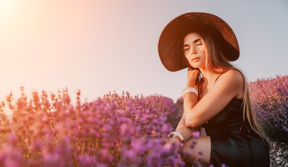 Woman lavender field. Happy carefree woman in black dress and hat with large brim walking in a lavender field during sunset. Perfect for inspirational and warm concepts in travel and wanderlust.