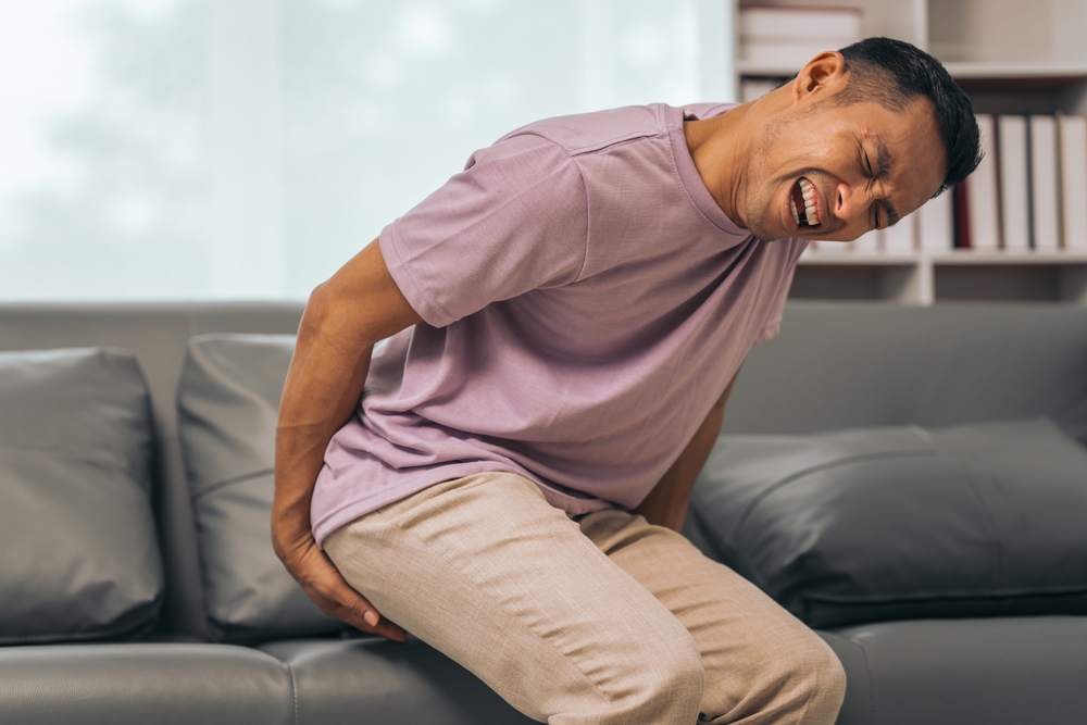 Middle-aged Asian Indian man with butt pain, hemorrhoids, colon pain, sitting on a sofa.