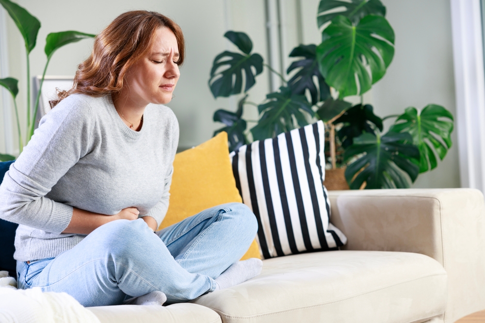 Young woman sitting on the couch at home with a pain in her stomach