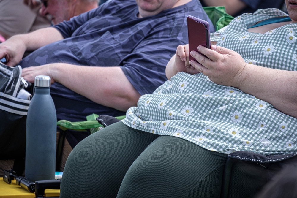 An obese man and woman sitting in chairs and looking at their smart phones. Summer holiday.