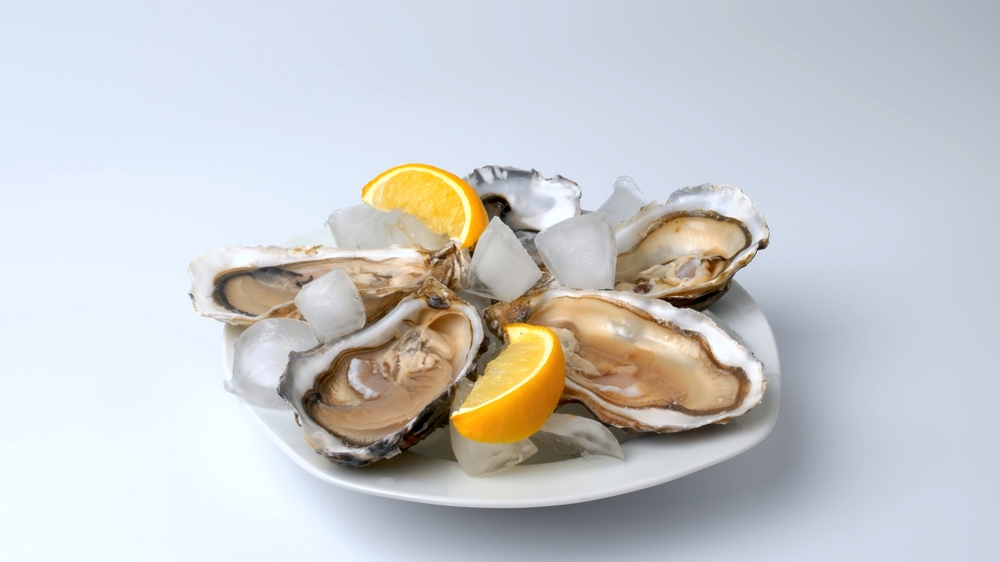 A plate of oysters with lemon on a gray background. Served with oysters and lemon. Fresh oysters close up. Healthy sea food. Oyster dinner in a restaurant. Oysters with lemon.