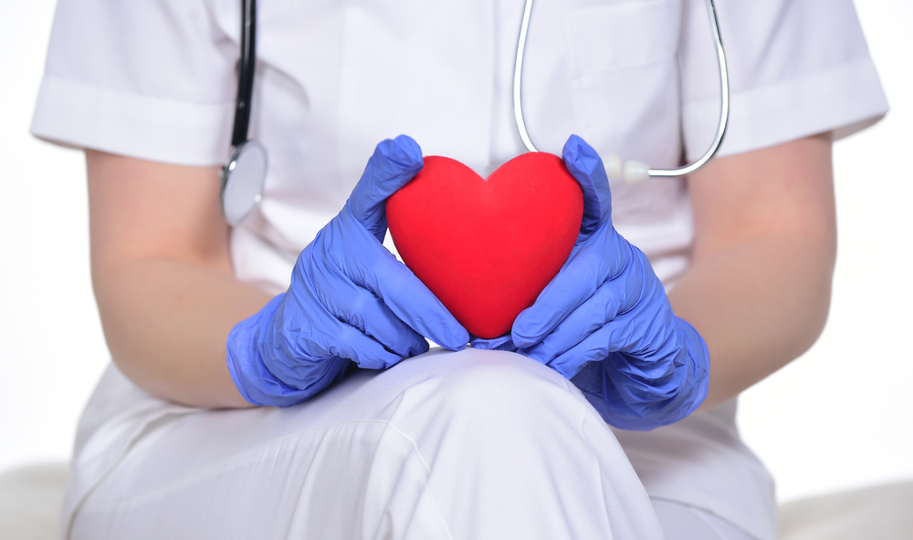 Close up of cardio heart surgeon hands holding red heart shape on white background