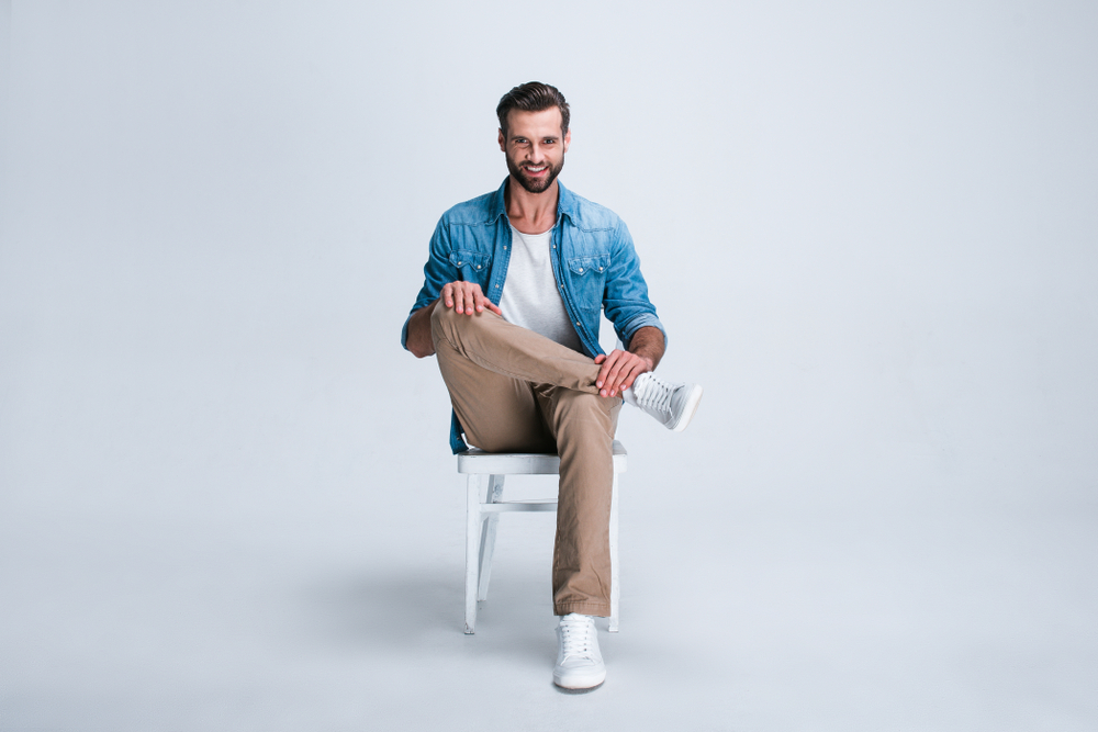 Feeling comfortable anywhere. Full length of handsome young man looking at camera with smile while sitting against white background
