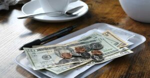 From Your Hair Dresser to a Barista, Here’s How Much You Should Tip in Every Situation cash tip left by customer at coffee shop
