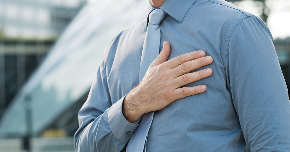 man wearing blue shirt and tie with hand placed over chest. Heart condition, heart health concept