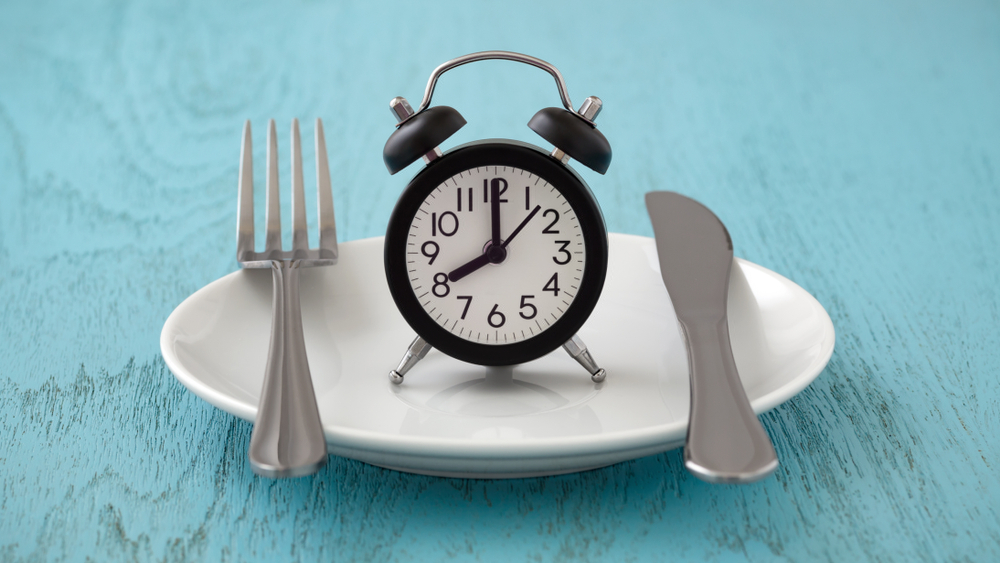 Clock on white plate with fork and knife, intermittent fasting, meal plan, weight loss concept on blue table