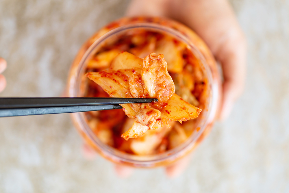 Kimchi cabbage in a bowl holding by hand with chopsticks for eating, Korean food, top view

