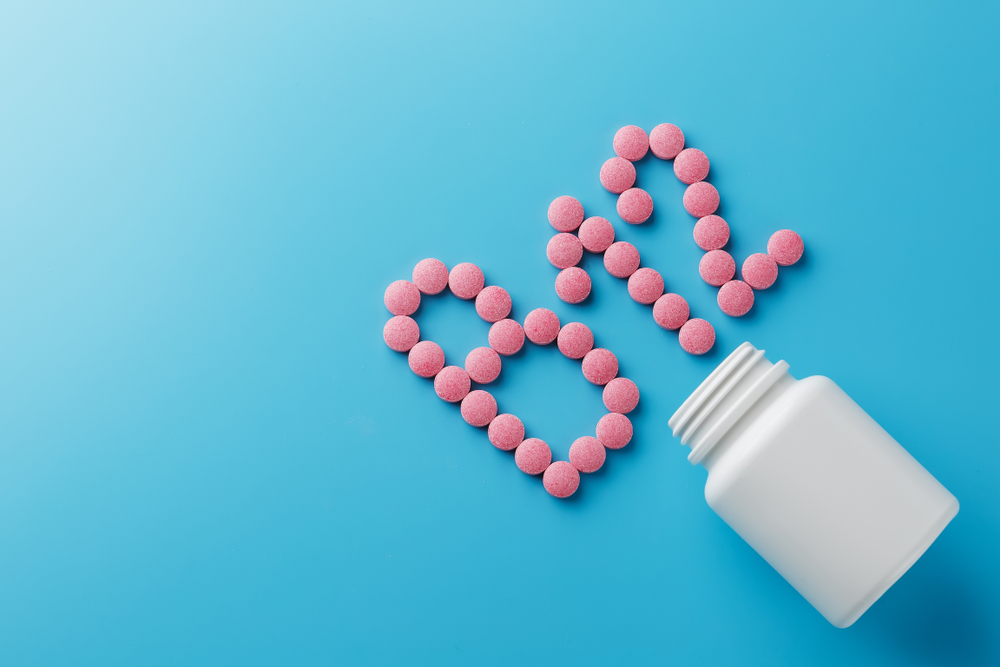 Pink round vitamins B12 shaped pills on a blue background spilled from a white can
