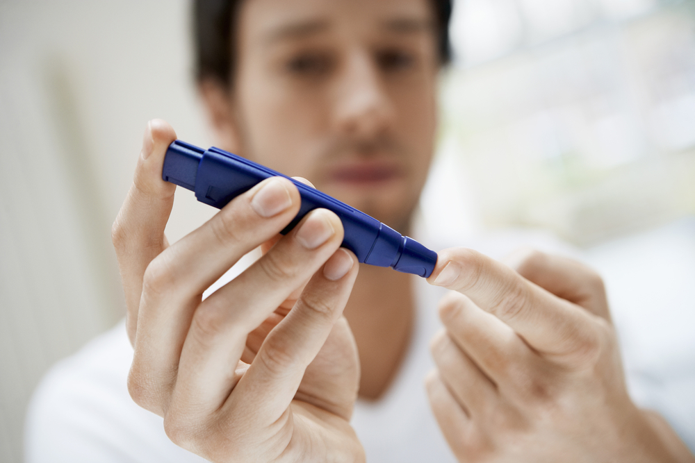 Closeup of young man using lancelet on finger in bathroom