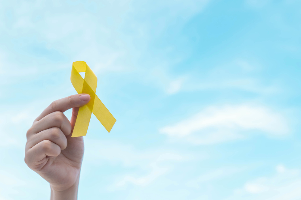 Hand holding yellow gold ribbon awareness over blue sky. Symbol for support suicide prevention, endometriosis, sarcoma bone cancer, bladder cancer, liver cancer and childhood cancer awareness concept.
