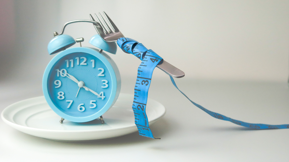 clock  and  fork with measuring tape  on white plate ,diet, weight loss, intermittent fasting concept.