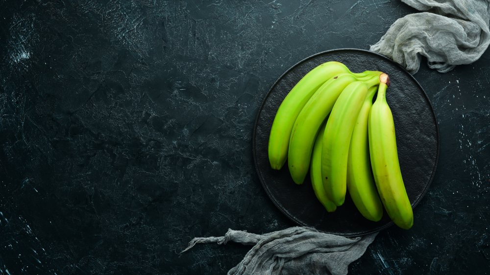 Fresh green bananas on black stone background. Top view. Free space for your text.