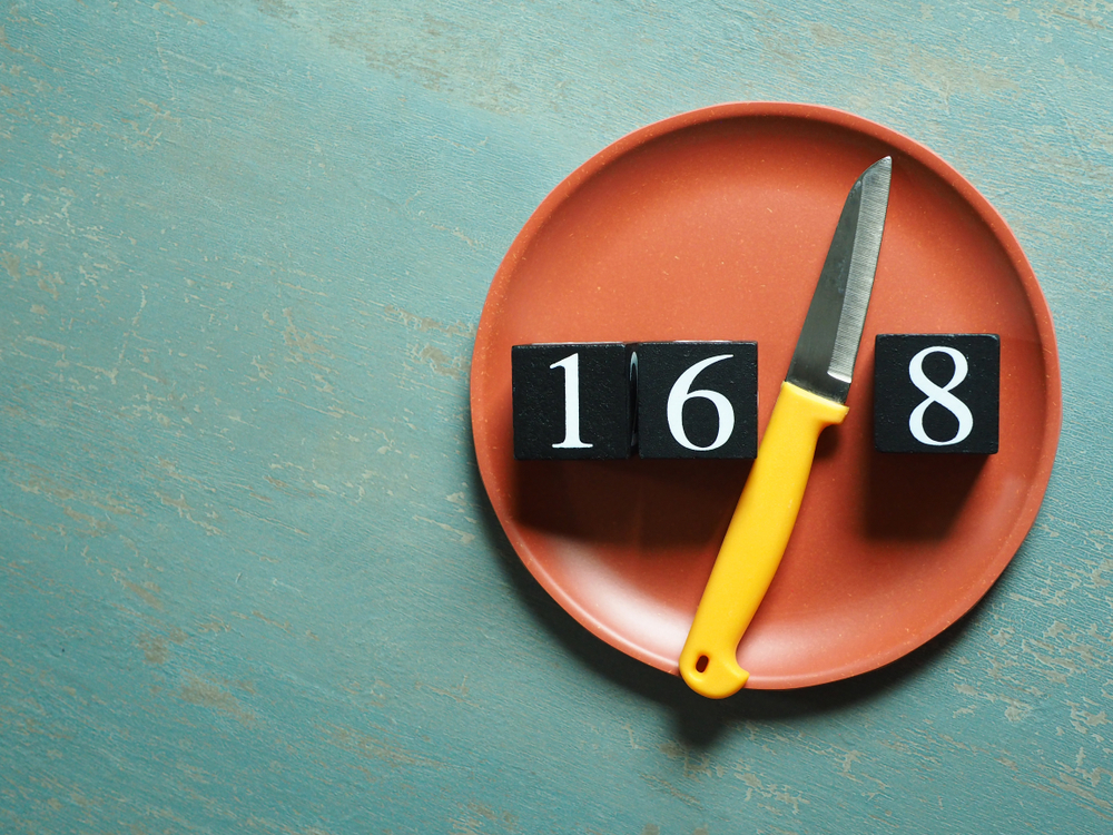 Intermittent Fasting theme represented by yellow knife between black painted wooden dice with white number 16 and 8 on red plate over vintage green background. Popular health and fitness trend.
