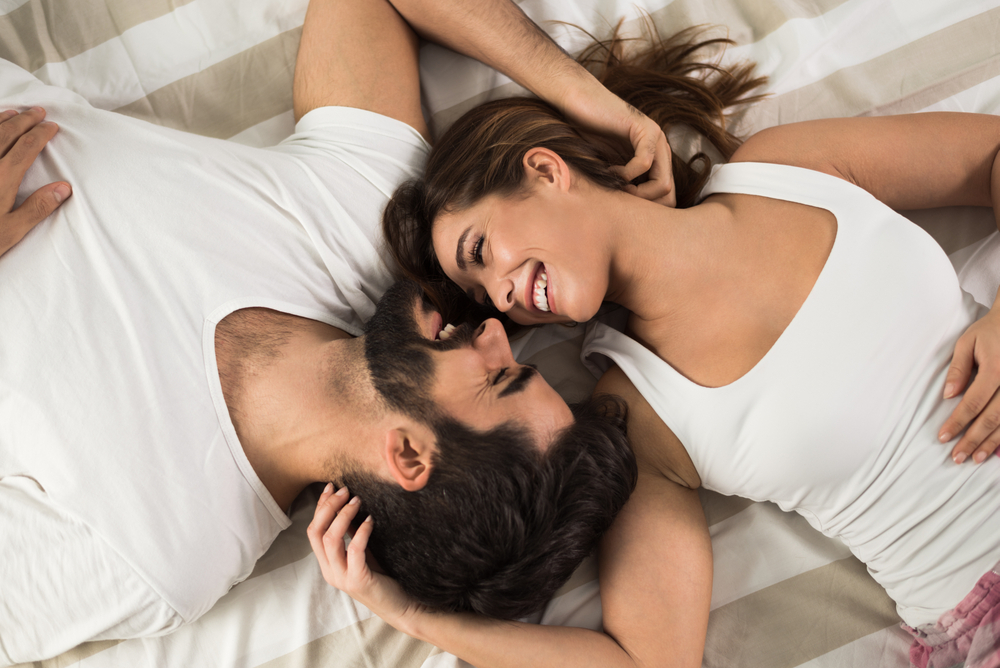High angle view of smiling couple relaxing and lying down in bed .They are looking at each other
