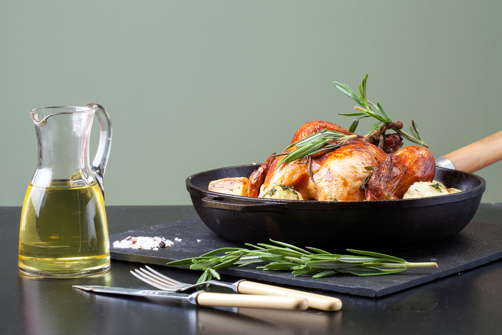Baked whole chicken with potatoes served in a cast-iron pan with rosemary and sea salt. Dark background, side view
