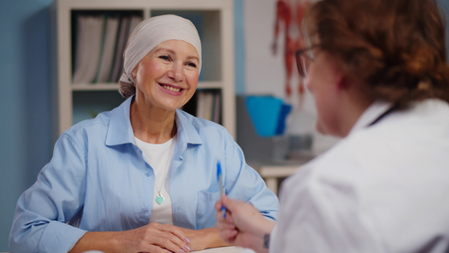 Mature woman with cancer visiting doctor in hospital listening about recovery. Back view of oncologist telling good news to patient after chemotherapy
