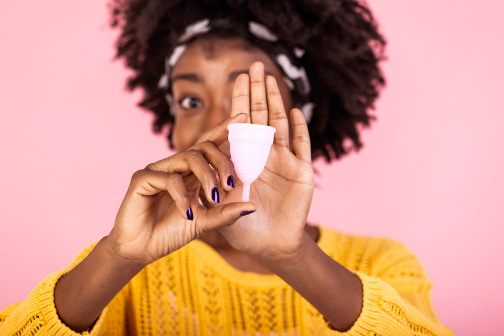Close up portrait of African American woman holding menstrual cup isolated over purple studio background, happy female, having period, dislike to use napkins or tampons
