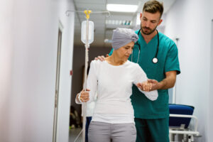 cancer patient connected to an IV being guided by a doctor or nurse through clinic hallway
