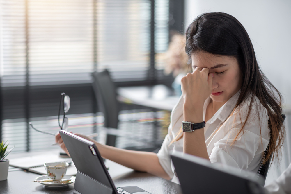 Image of an Asian business woman is stressed, bored, and overthinking from working on a tablet at the office.
