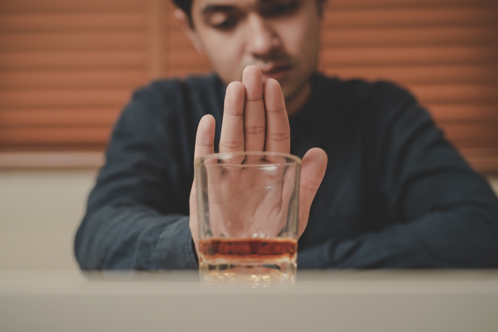 Alcoholism, sad depressed asian young man refuse, push alcoholic beverage glass, drink whiskey, sitting alone at night. Treatment of alcohol addiction, having suffer abuse problem alcoholism concept.
