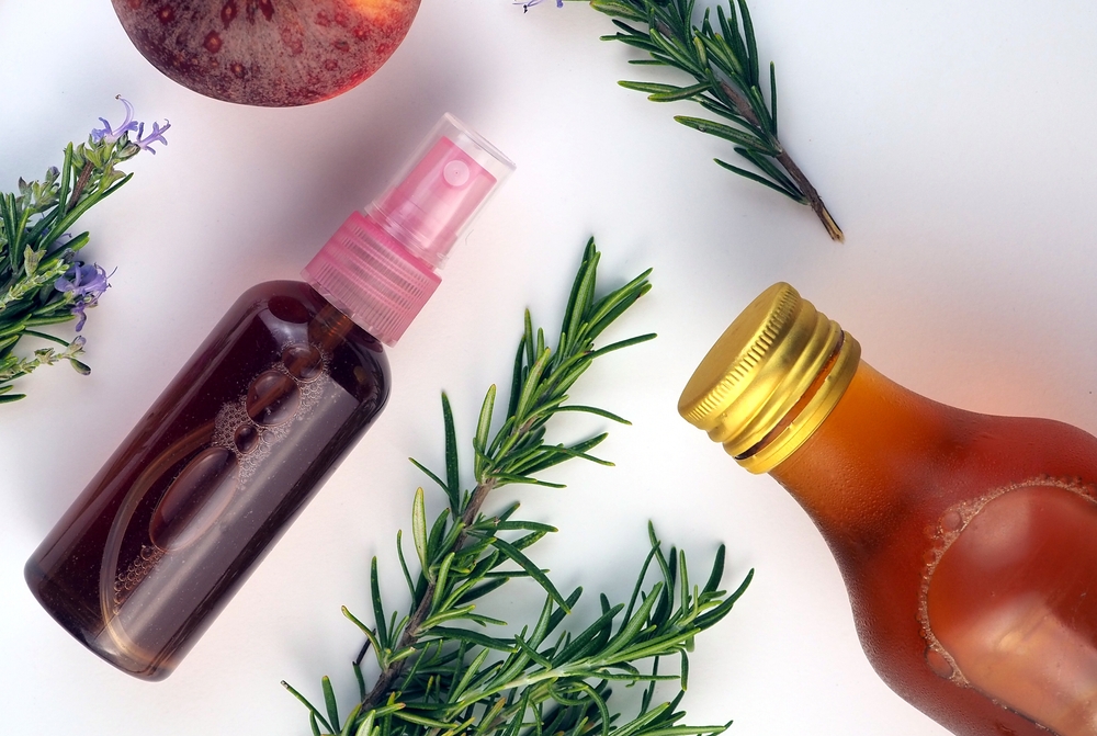 Rosemary and apple cider vinegar face toner in a bottle with spay, rosemary branches, apple cider vinegar bottle on white background. Flat lay