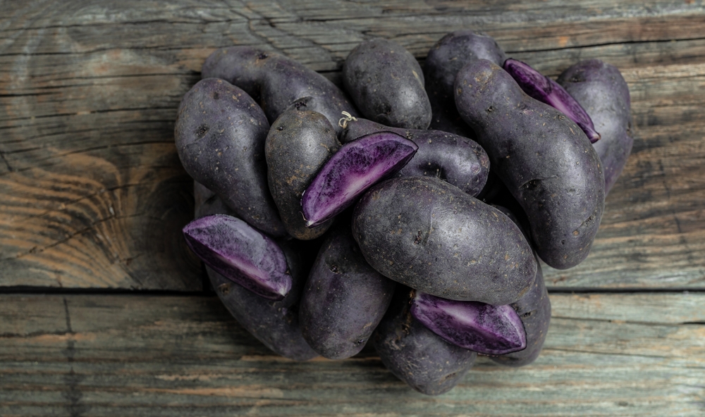 Raw purple sweet potato food . Fresh potatoes in an old sack on wooden background. Batata potato. vegan food ingredient. banner, menu, recipe place for text, top view.
