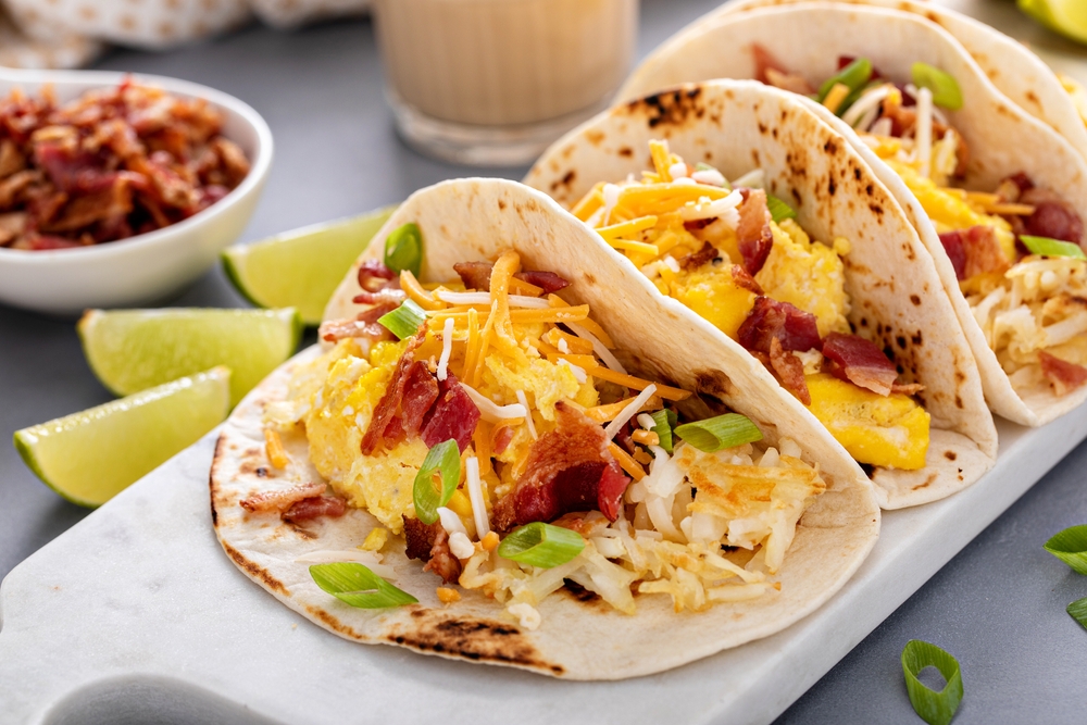 Breakfast tacos with hashbrowns, scrambled eggs and bacon topped with cheese and green onion