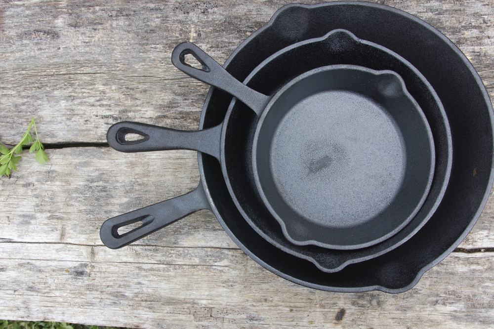 Three cast iron pans placed one inside the other on a wooden table. Cast iron cookware of various sizes used for rustic cuisine cooking.

