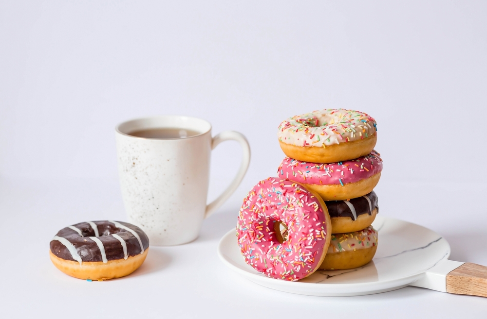 Delicious dessert. Pink, white and chocolate donuts with multicolored sprinkles, a cup of black coffee or tea. Sweets.