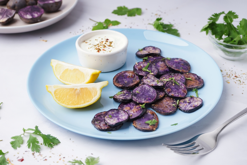 Plate with slices of fried purple potatoes, lemon and sauce on light background
