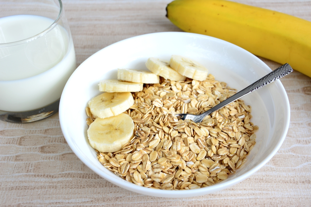 oat flakes with banana slices, teaspoon, yellow banana and glass of milk, close-up