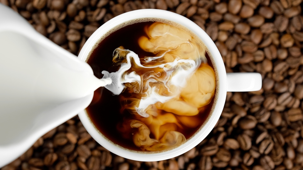 Pouring milk in coffee cup, top view