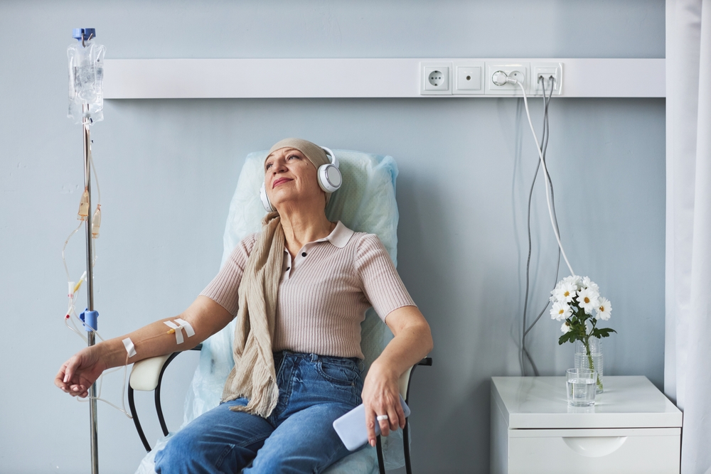 Portrait of senior woman sitting in comfortable chair with IV drip and listening to music during chemotherapy treatment, copy space