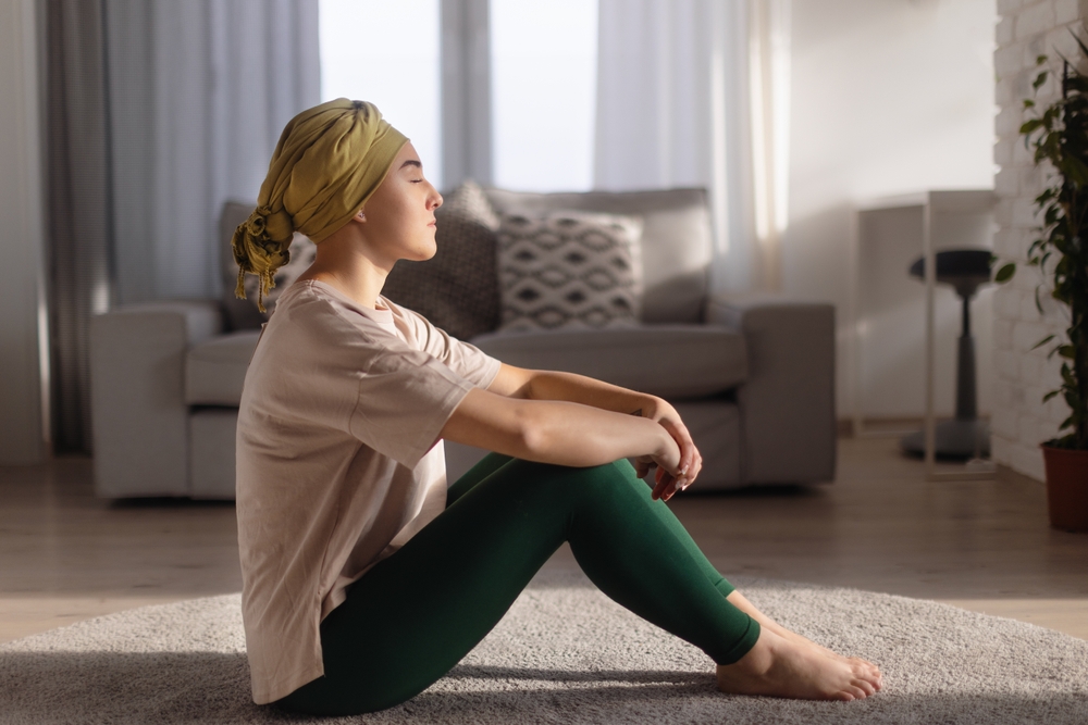 Young woman with cancer sitting after doing yoga in her apartment.
