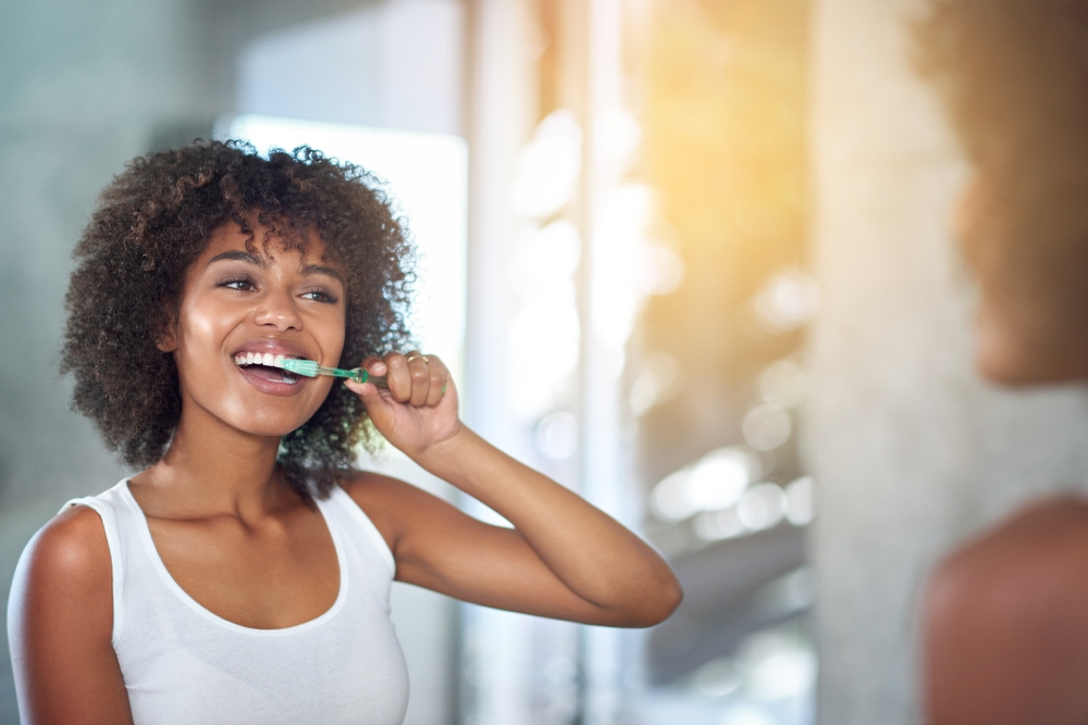 Mirror, dental and black woman brushing teeth, fresh breath and oral health in the bathroom. Female person, happy model and lady with wellness, mirror and hygiene with morning routine and tooth care
