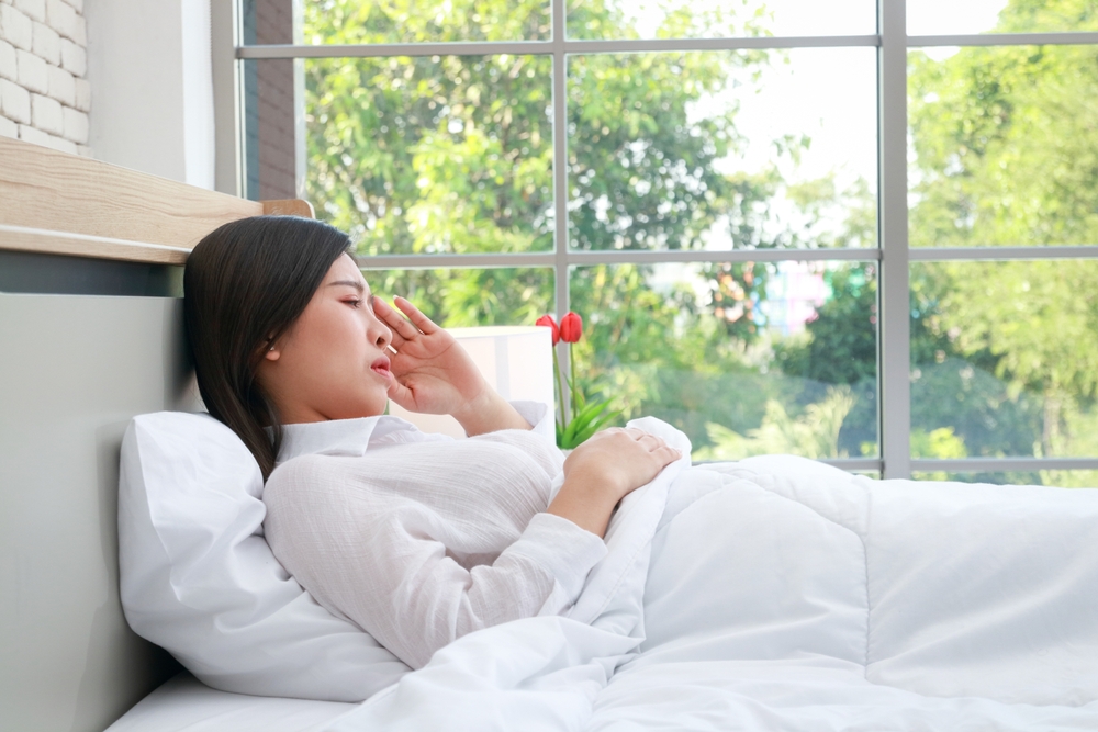Asian woman is sick and has a headache. She is resting in bed. Health concept. Flu caused by a virus
