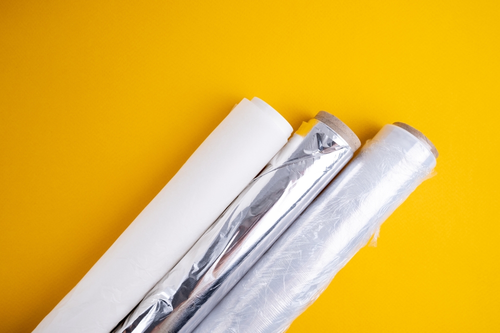 Plastic wrap, aluminum foil and a roll of parchment paper on a yellow background. Gadgets for the kitchen and packaging